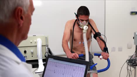 hombre en forma haciendo una prueba de estrés en una bicicleta de ejercicio observado por un médico