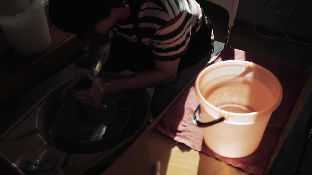 un alfarero trabaja y hay un cubo de agua al lado para mojar la arcilla