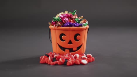 Scary-halloween-pumpkin-printed-bucket-full-of-candies-against-grey-background