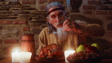 starving nobleman tears off chicken leg at medieval dinner. mature aristocrat eats poultry meat and grape at dining table in tavern. king banquet guest