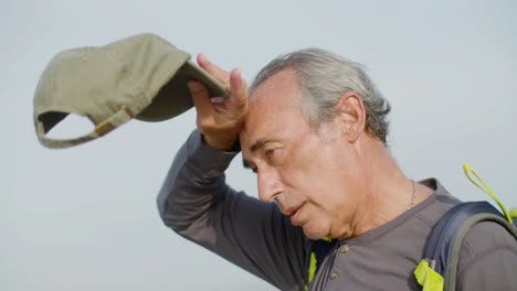 medium shot of a tired hard-breathing hiker wiping sweat from forehead