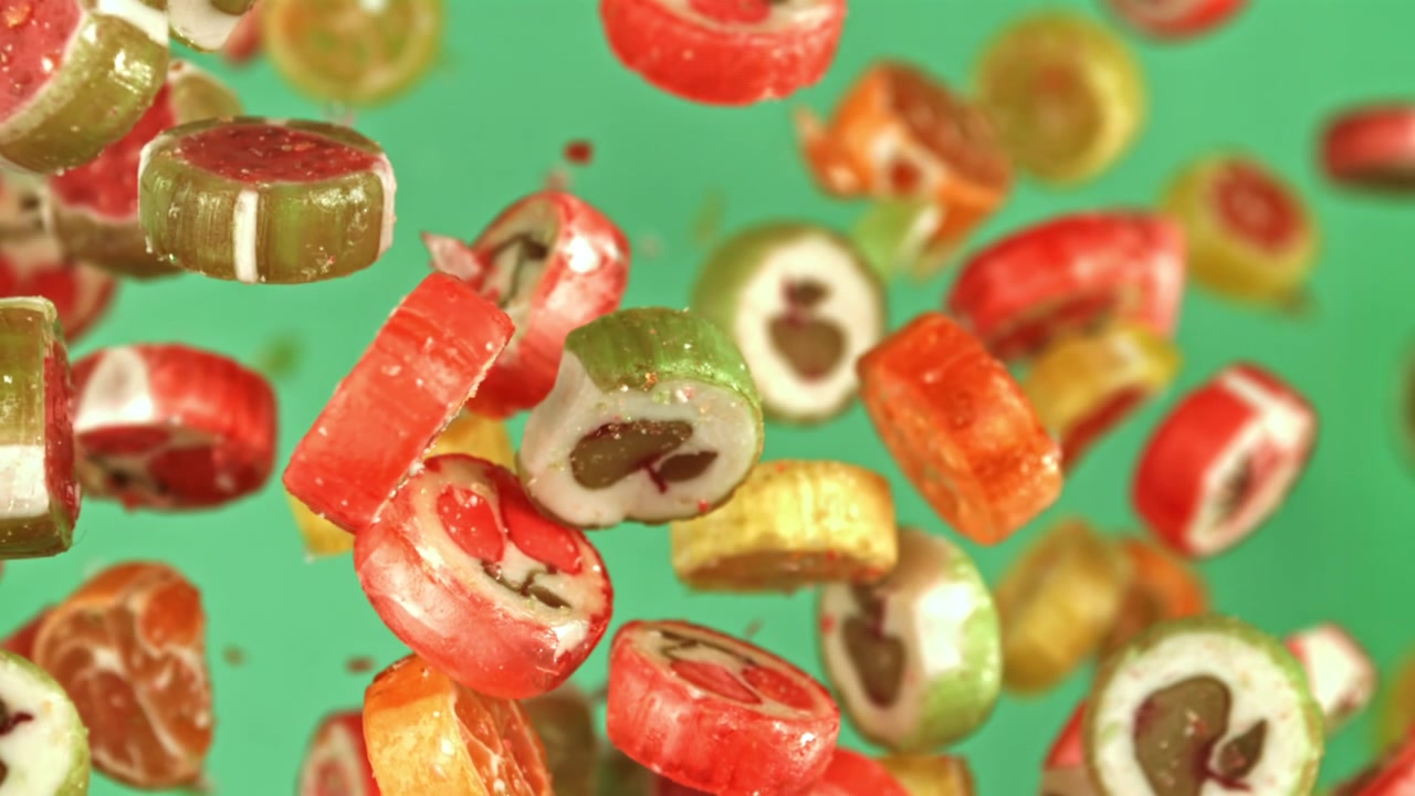 Bunte Fruchtbonbons fallen in Zeitlupe auf grünem Hintergrund