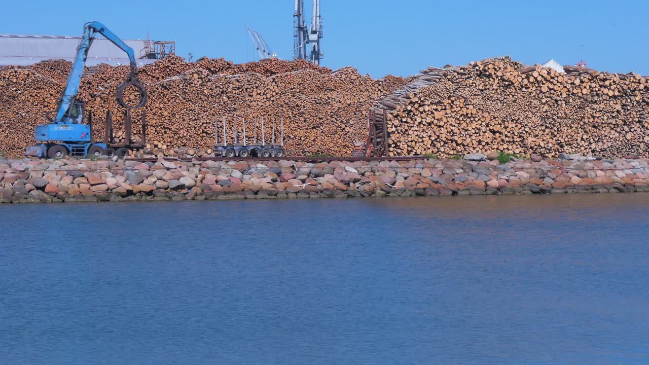 camión de carga forestal azul que trabaja en la terminal de carga seca en el puerto de liepaja en un día soleado con cielo despejado, plano amplio sobre el canal del puerto
