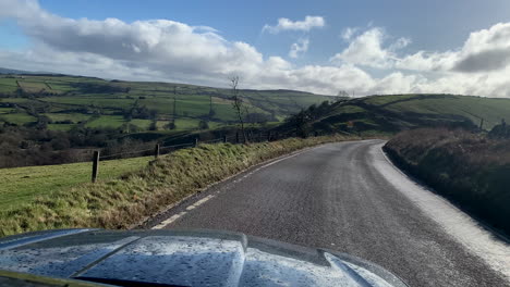 A-car-diving-alaong-a-road-in-the-countryside-with-rolling-hills-in-the-distance