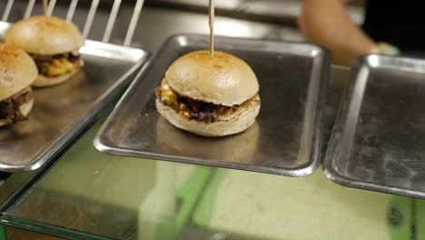 Chef-placing-freshly-cooked-burgers-on-metal-trays,-close-up-motion-shot