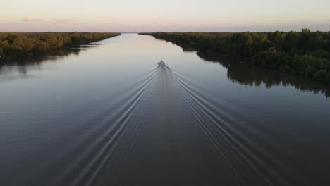 aerial shot of cruising speed boat on calm amazon river moving away during epic sunset at background