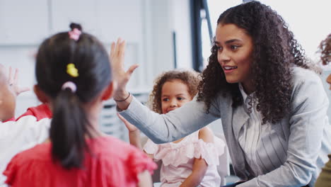 Infant-school-kids-giving-their-teacher-a-high-five-in-the-classroom-after-learning,-selective-focus