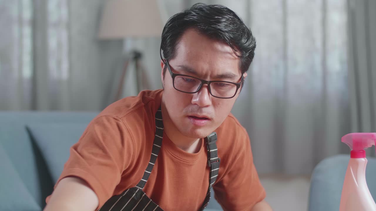 집에서 스프레이로 테이블을 청소하는 아프론을 입은 피곤한 아시아 남성 집무원