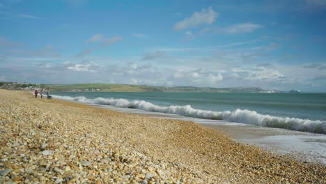 4K-Landscape-panoramic-shot-of-a-family-playing-on-the-beach-and-throwing-rocks-into-the-ocean