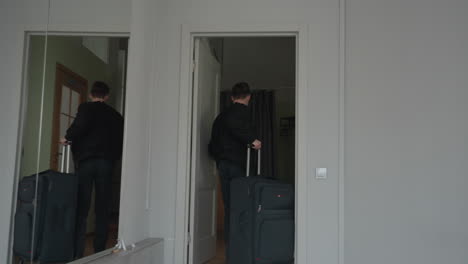 sport man seen from behind enters apartment wearing black jacket after returning from sport trip, facing closed white door with large mirror on wall reflecting hallway and neutral toned interior