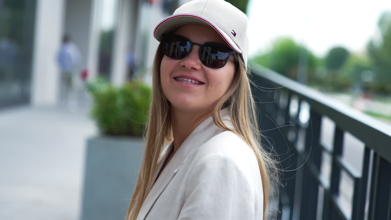 Smiling happy woman in black sunglasses and cap outdoors. Stylish fashionable young lady in the urban surrounding. Close up portrait.