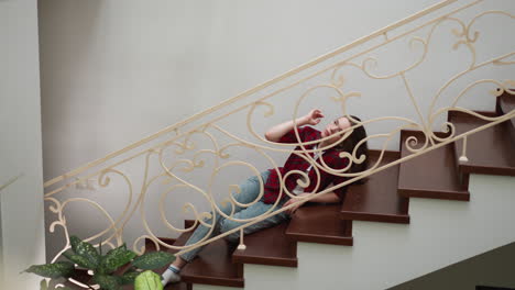 exhausted woman strokes head lying on steps. frustrated lady does self calming motions to deal with stress on stairs. mental health care importance