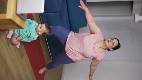 Overweight-woman-performing-yoga-asana-warrior-at-home-with-her-baby-on-the-floor