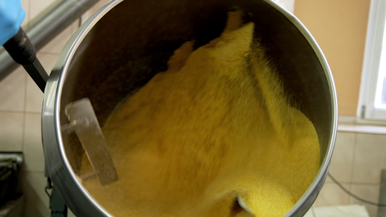Yellow substance being mixed in a big metal tank. Sweet corn desserts production at the food factory.