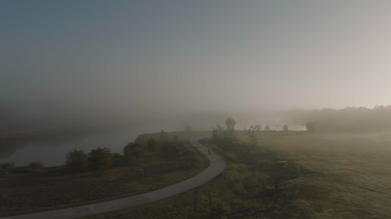 A 4K aerial drone view of an adult male walking into fog and mist in the early morning at Exploration Green in Clear Lake, Houston, Texas.