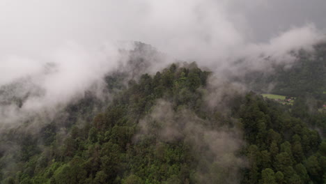 Aerial-shot-of-mountain-with-trees-covered-in-clouds-with-a-small-town-in-the-background-in-Valle-De-Bravo,-Mexico