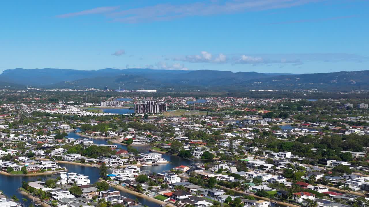Aerial footage of Gold Coast, Australia, showcasing urban sprawl, waterways, and distant mountains under clear blue skies