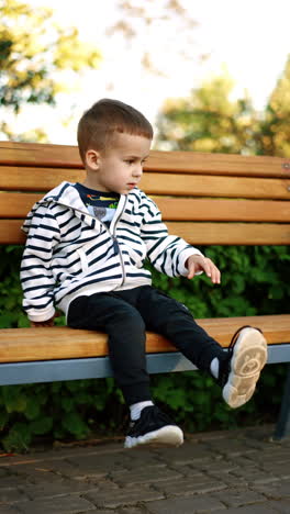 cute caucasian baby sitting on the bench outdoors. kid showing his age on the fingers and waves his feet. vertical video.