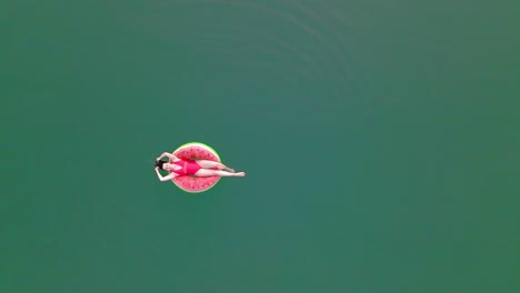 overhead top view of woman swimming with watermelon swimming circle in blue water