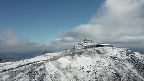 Drone-shot-of-a-snowy-Snowdon-mountain-with-small-cabin-on-the-top-under-a-clear-sky-in-UK