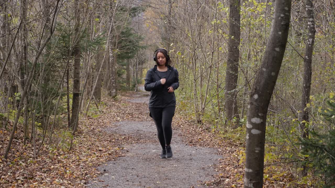 Una donna indossa le cuffie e inizia a fare jogging su un piccolo sentiero attraverso il bosco