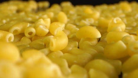 dolly shot of coquillettes or cornettes pasta on black table