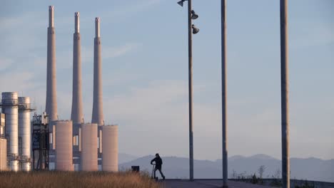 hombre contemplando el paisaje industrial monta en scooter eléctrico al atardecer