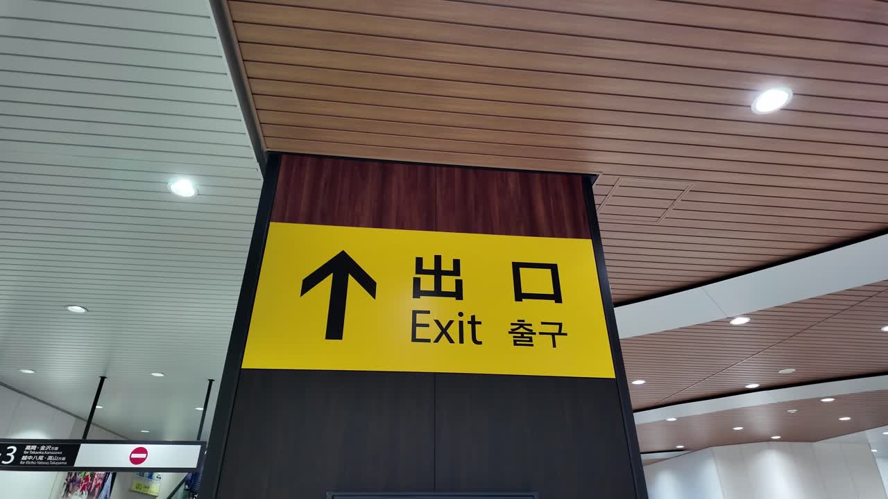 Yellow exit sign with arrow and Japanese and English words at Toyama Station, Japan, guiding people towards safety and escape route. pan right