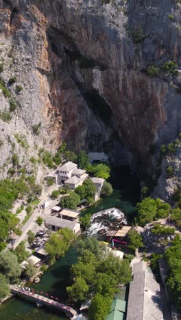 drone reveals the blagaj tekija monastery by cliff and spring fed buna river in serene bosnia, aerial pullback establishing reveal, vertical