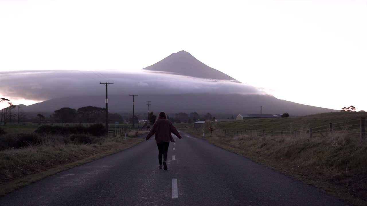 Woman Walking on Road Towards Mountain