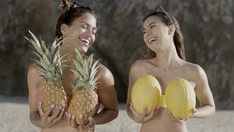 vista frontal de mujeres sonrientes con piñas y melones en la playa