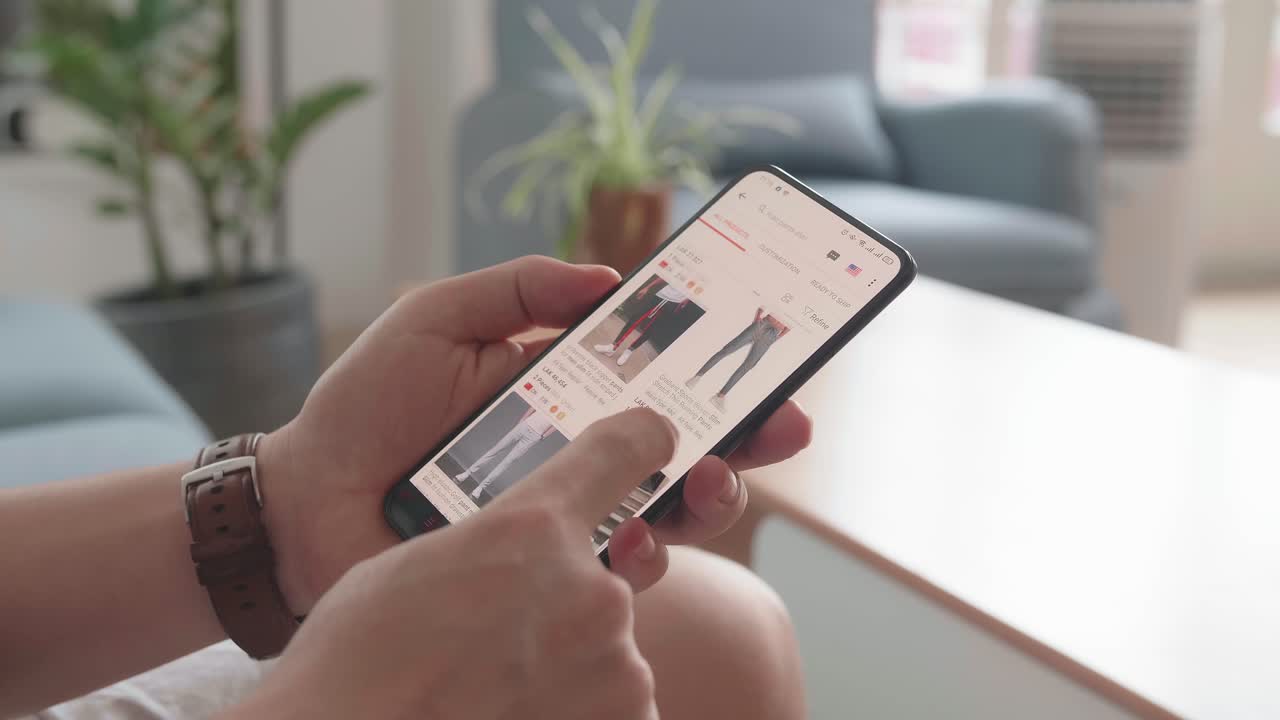 Close Up Of Man Hand Holding Smartphone And Doing Online Shopping At Home, Male Looks At Goods In Online Store Clothing