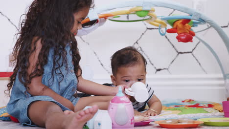 Young-girl-playing-tea-party-sitting-on-the-floor-with-her-baby-brother-lying--beside-her