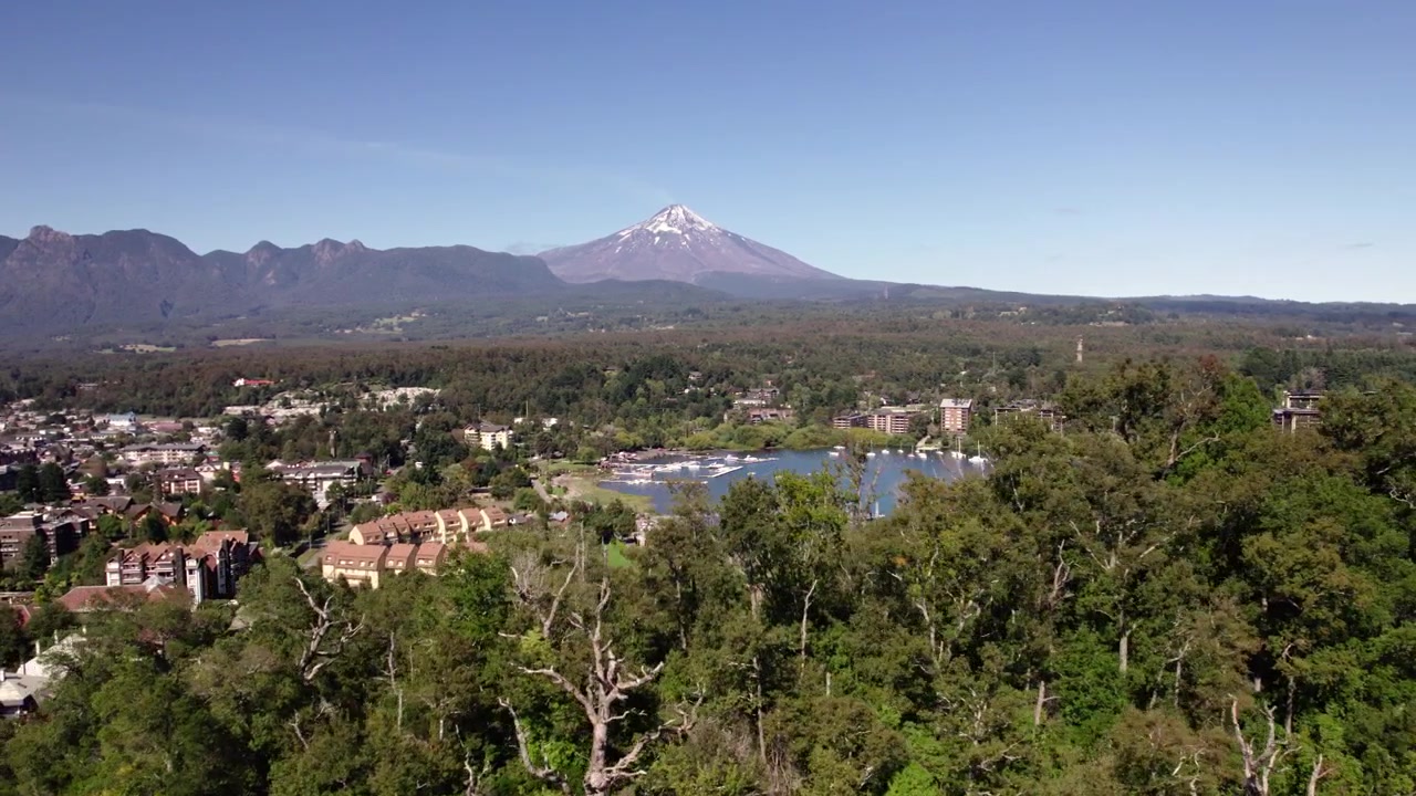 Vista aerea della città di Pucón in Cile con montagne e un vulcano innevato sullo sfondo sotto un cielo azzurro limpido
