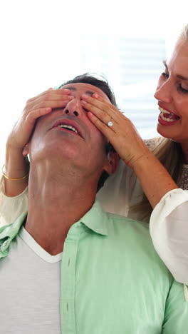 mujer sonriente cubriendo los ojos del hombre en la sala de estar en casa