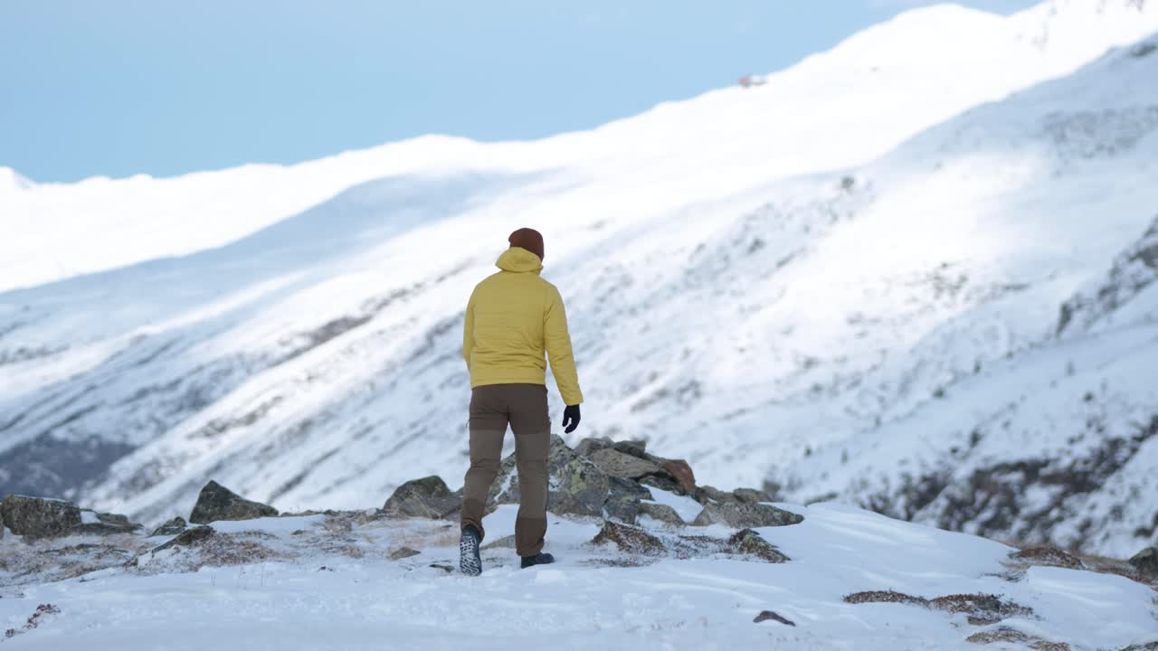 노란색 재킷을 입은 백인 청년과 비니를 걸고 스위스 플루엘라 패스에 있는 산골짜기의 전망을 보기 위해 멈춥니다