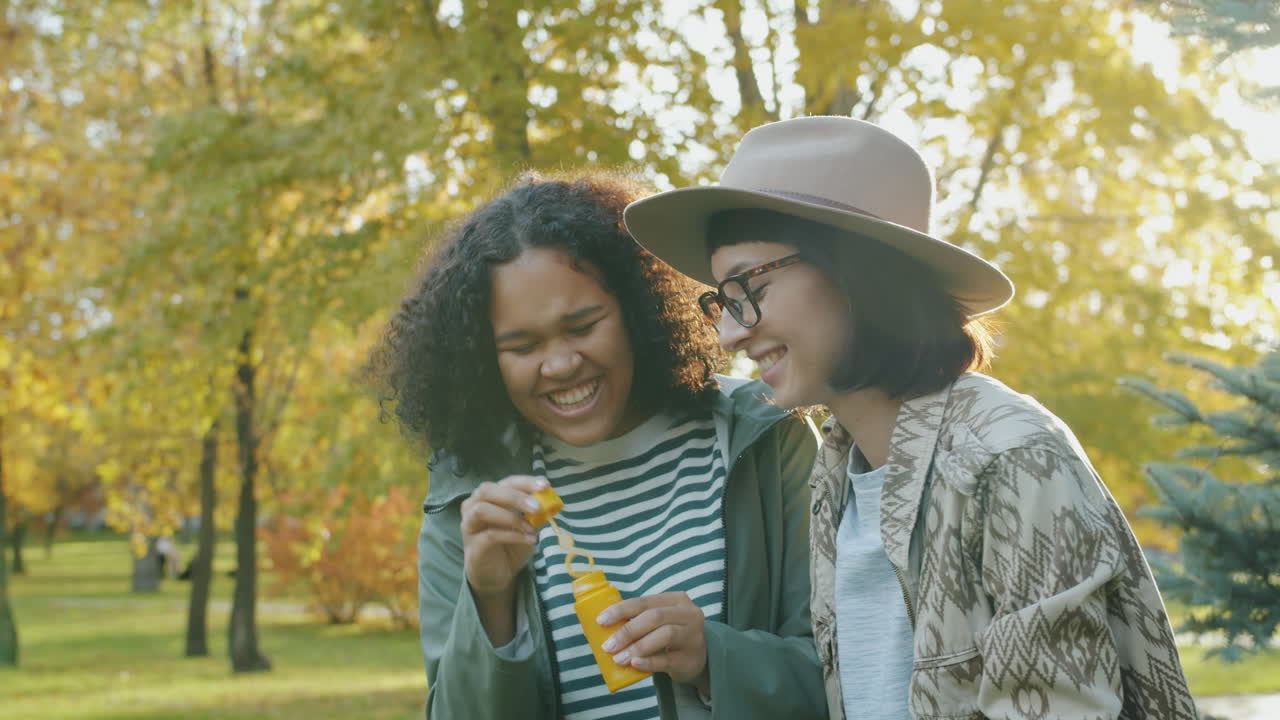 Two friends having fun with bubbles in the park during autumn
