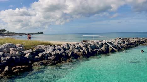 Couple-walking-on-a-sandy-beach-near-rocks-and-clear-turquoise-water-4K-30-FPS