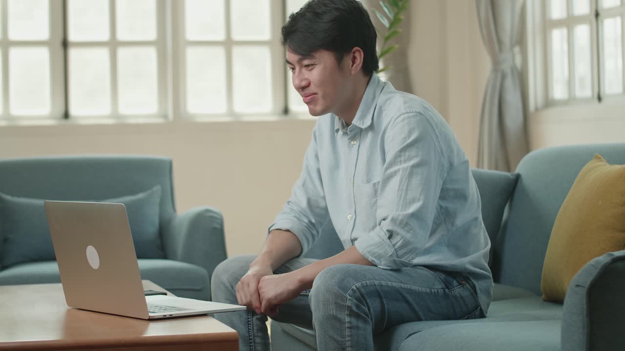 Asian Man Greeting With Colleagues In Video Conference Call From Laptop At Living Room, Video In 4K