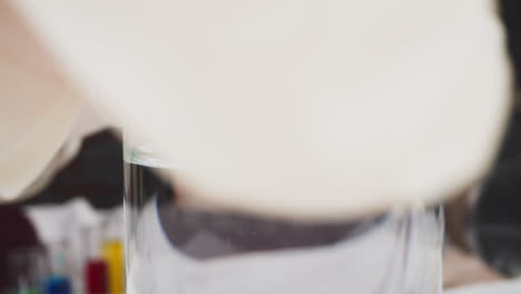 worker in gloves puts beaker with liquid in front of camera