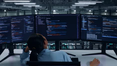 vista trasera de una mujer asiática aburrida desarrolladora escribe código con múltiples pantallas de computadora en el centro de datos