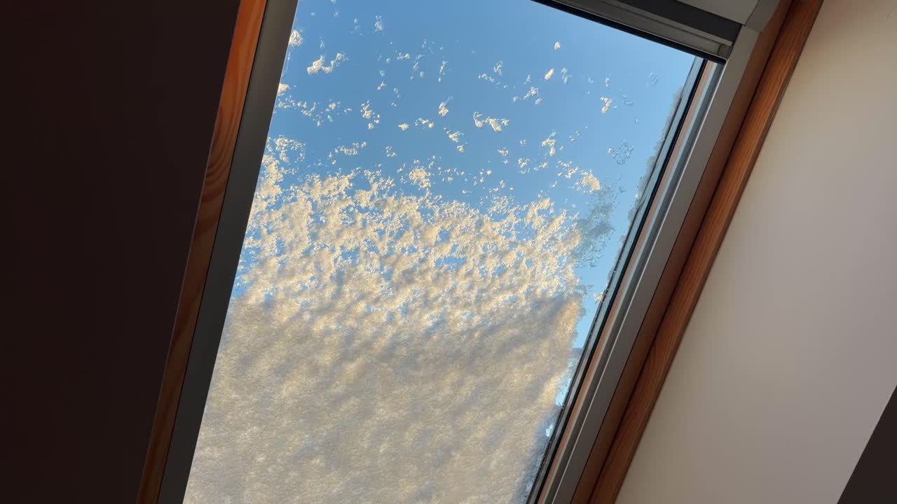 Finestra di una soffitta innevata durante l'inverno, neve che cade e condizioni di ghiaccio che creano un'atmosfera fredda e isolata