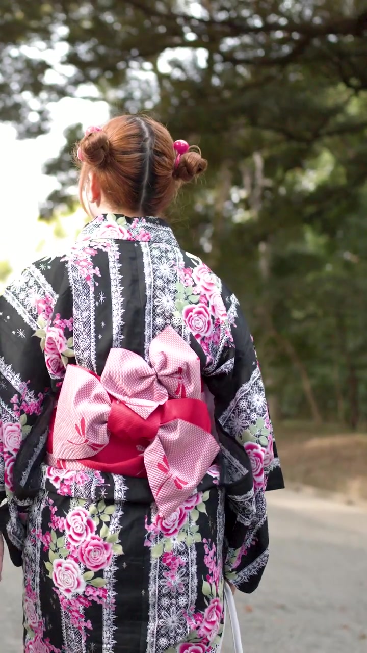 Uma mulher vestindo um yukata floral tradicional caminha por um parque durante um festival de verão.
