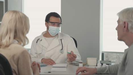 a young black doctor in a facemask talking to a ederly couple