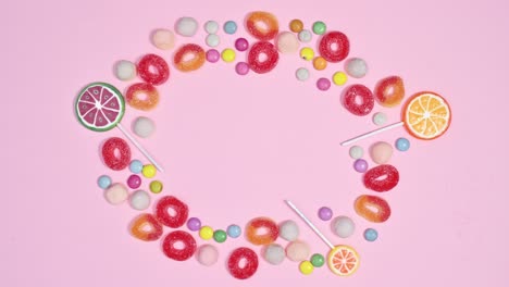 sweet gummy candies, chocolate candies and lollypops appear in circle making frame on pastel pink background. stop motion animation flat lay