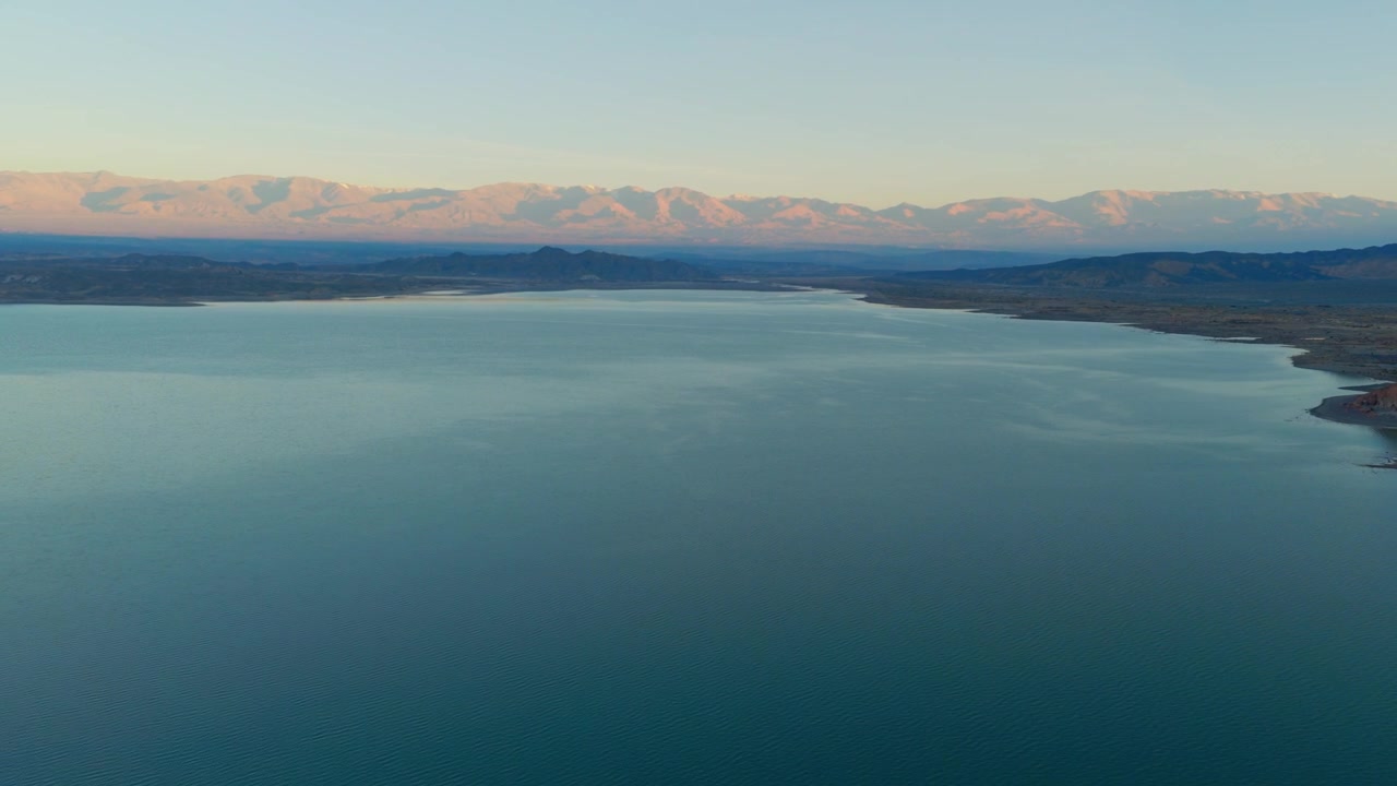 Široký záběr z dronu zleva nad velkým jezerem s horami v pozadí během východu slunce v Argentině