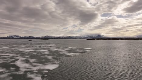 aerial icy lake mývatn meets snow peaks and cloudy sky near skútustaðir in reykjahlíð iceland