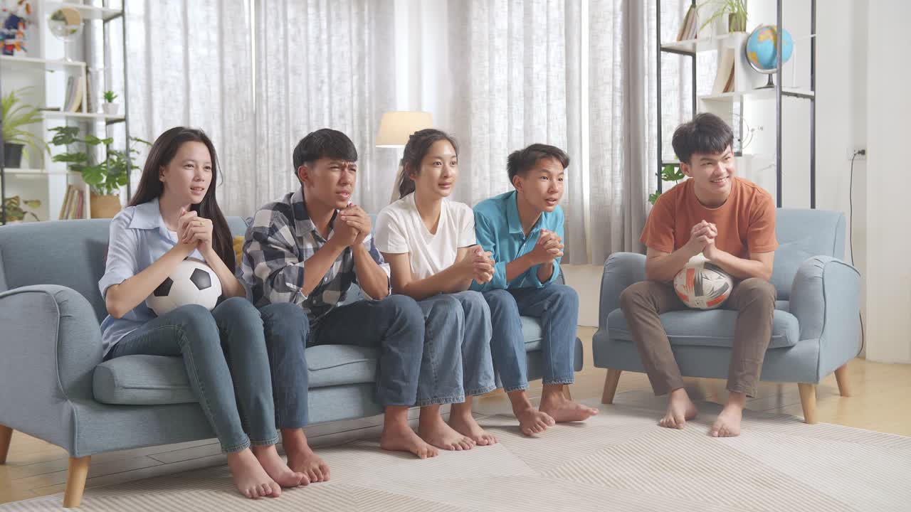 아시아 십대들이 tv에서 축구 경기를 지켜보고 집에서 승리를 축하하고 있습니다.