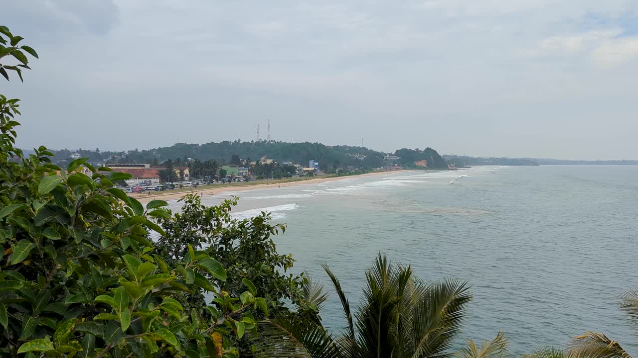 Glimpse of scenic sandy beach and ocean from behind green trees in southern Sri Lanka