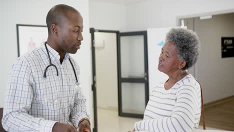 African-american-male-doctor-talking-with-senior-woman-in-hospital,-slow-motion